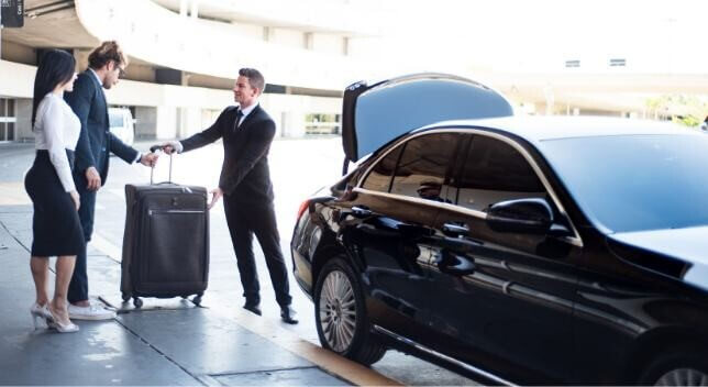 Chauffeur putting luggage into limousine trunk.