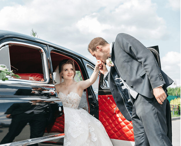 Groom kisses bride's hand in car.