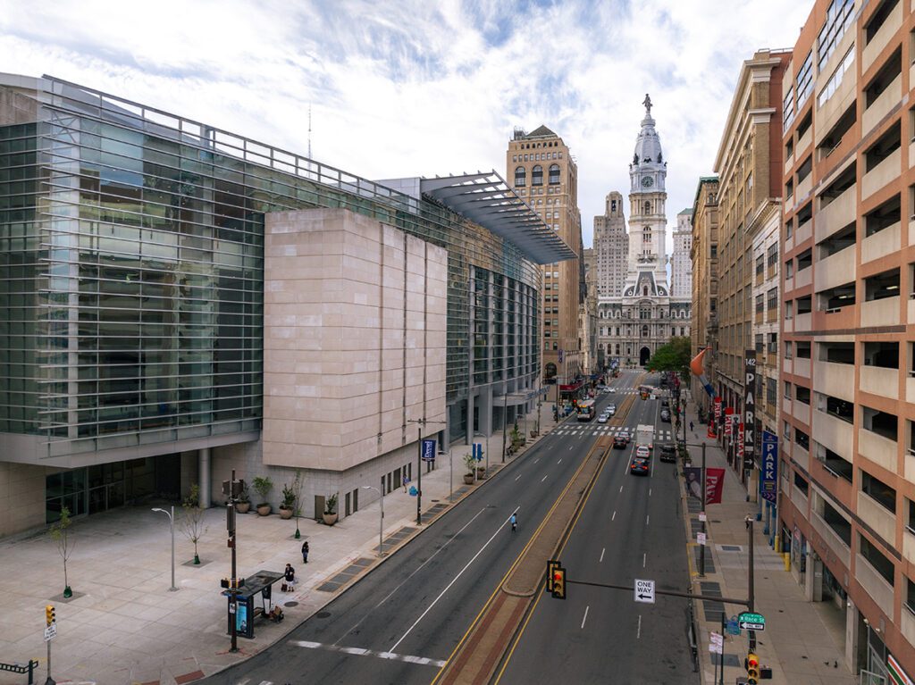 Wide city street with a glass-fronted building on the left and a ornate historic tower in the distance.