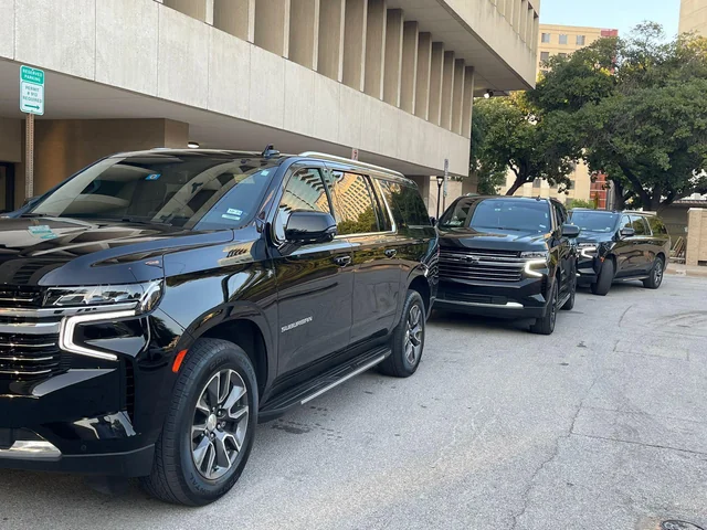 Line of black SUVs parked in a row along a curb beside a concrete building.
