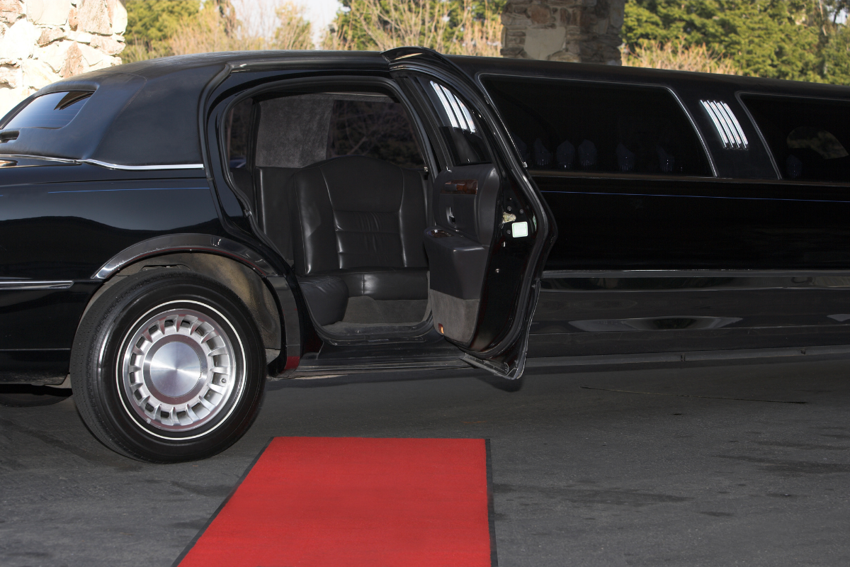 Black stretch limousine with the rear passenger door open, showing leather seats inside beside a red carpet.