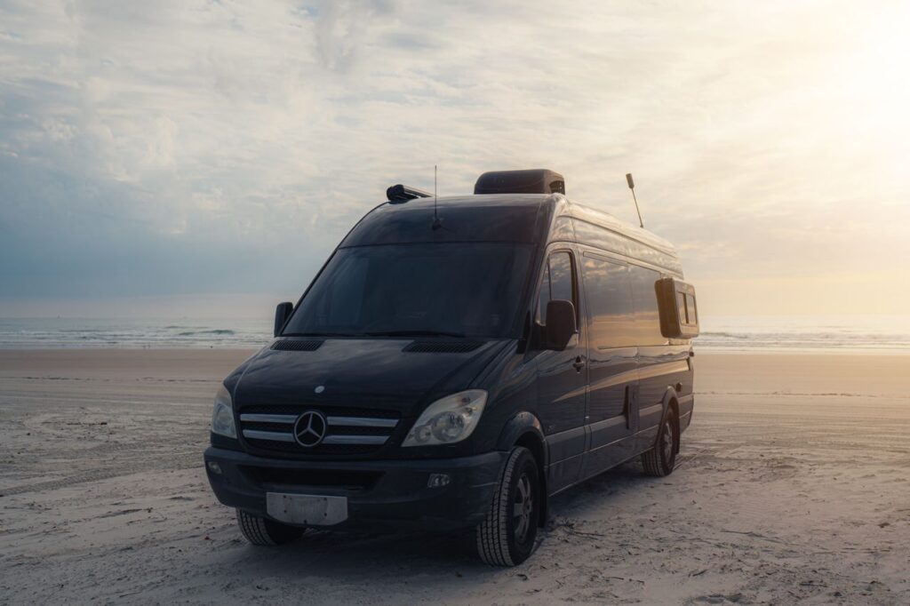 A black camper van parked on a serene beach during a beautiful sunset.
