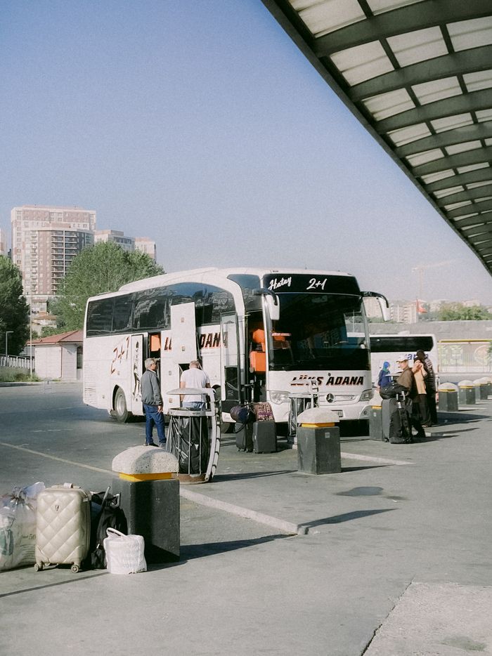 Travelers at a bus station boarding a bus on a sunny day.