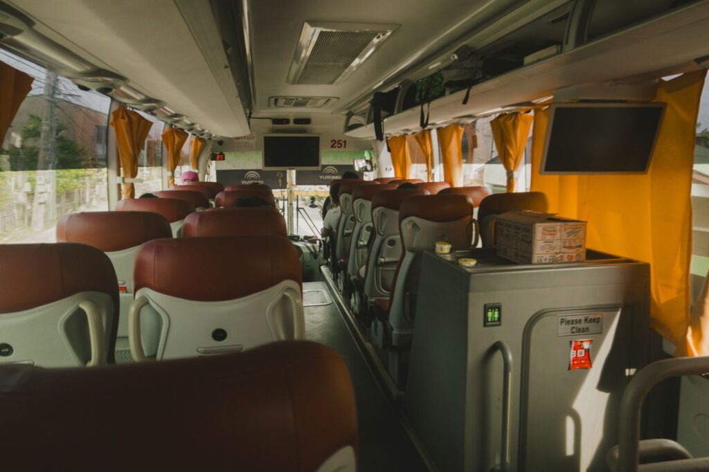 Spacious bus interior with plush seats, TV screens, and yellow curtains for a relaxing travel experience.