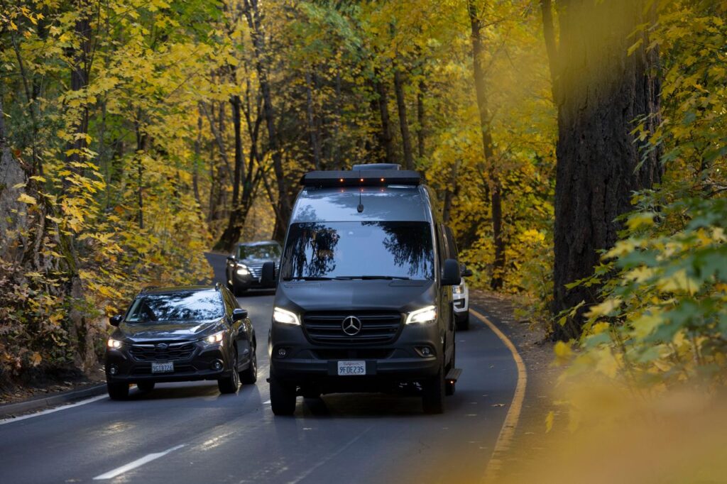 Vehicles navigate a scenic forest road during fall, surrounded by vibrant foliage.
