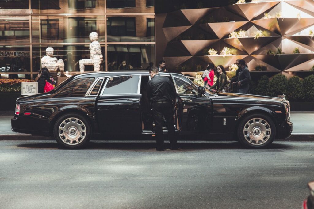 Black luxury stretch limousine with a chauffeur opening the rear door on a city street.